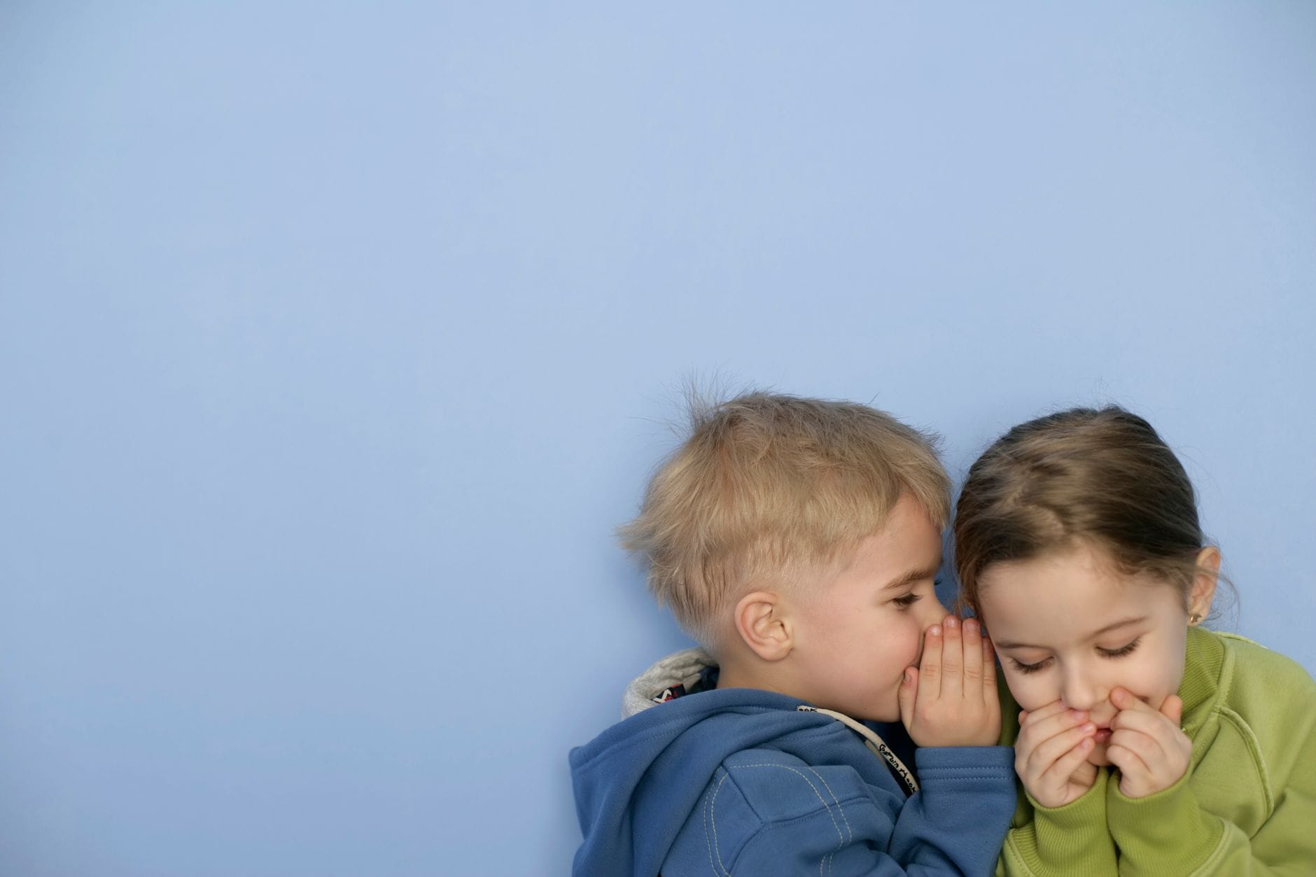 Dwoje małych dzieci szepcze sobie sekrety na jasnoniebieskim tle